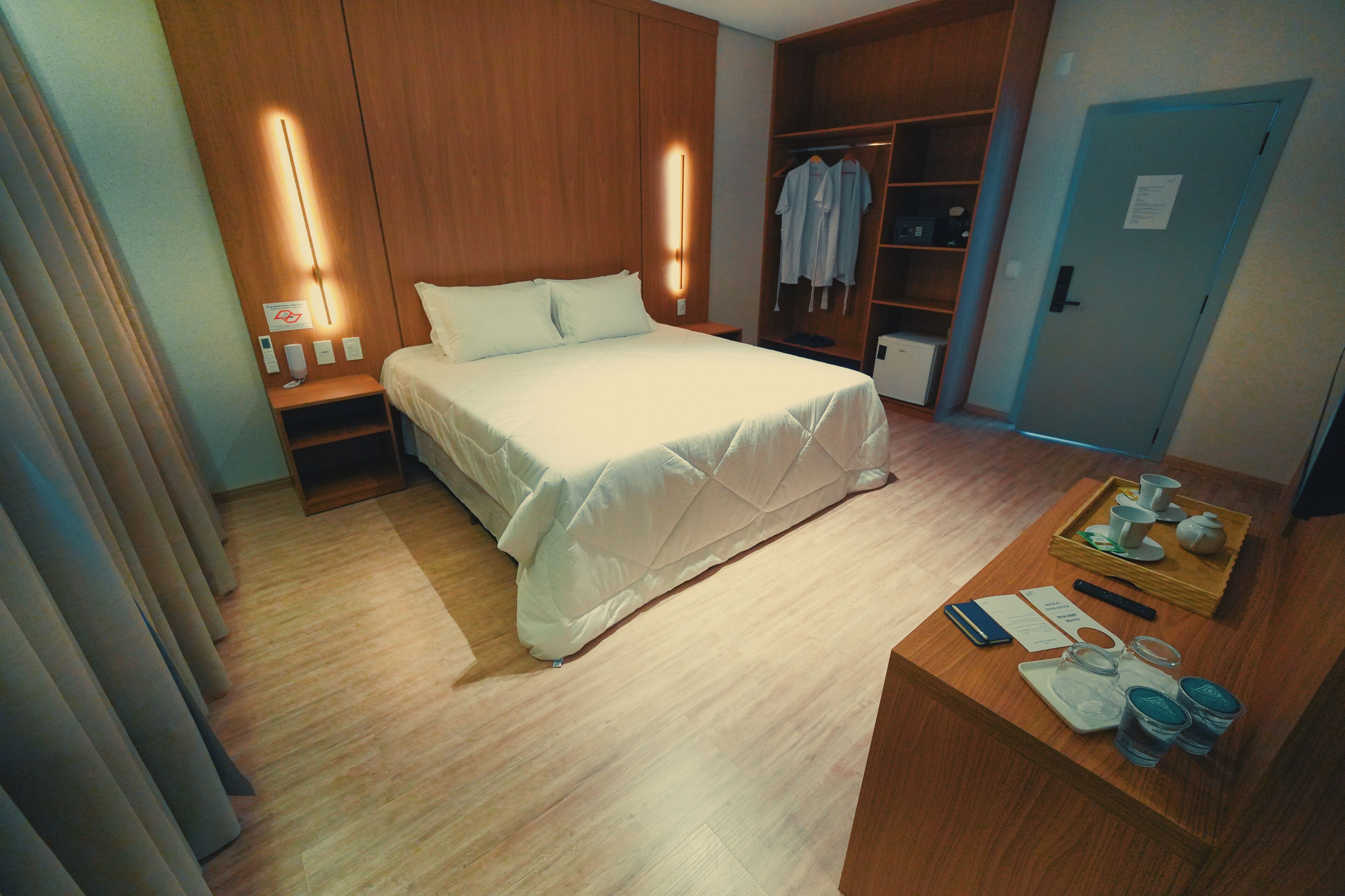 A hotel room with a bed, bedside table, wardrobe, and a tray table with items.