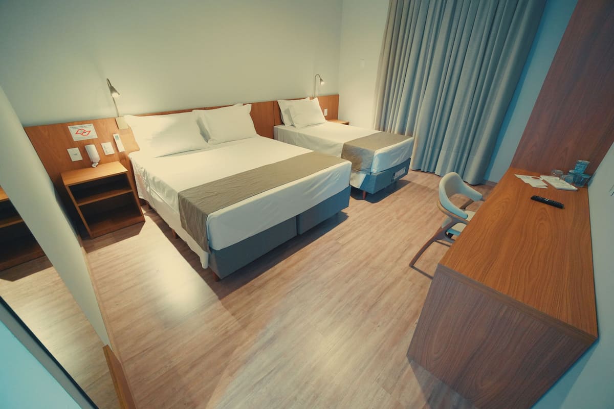 Une chambre d’hôtel avec deux lits, un bureau, une chaise, une lampe, une table de chevet et un rideau.