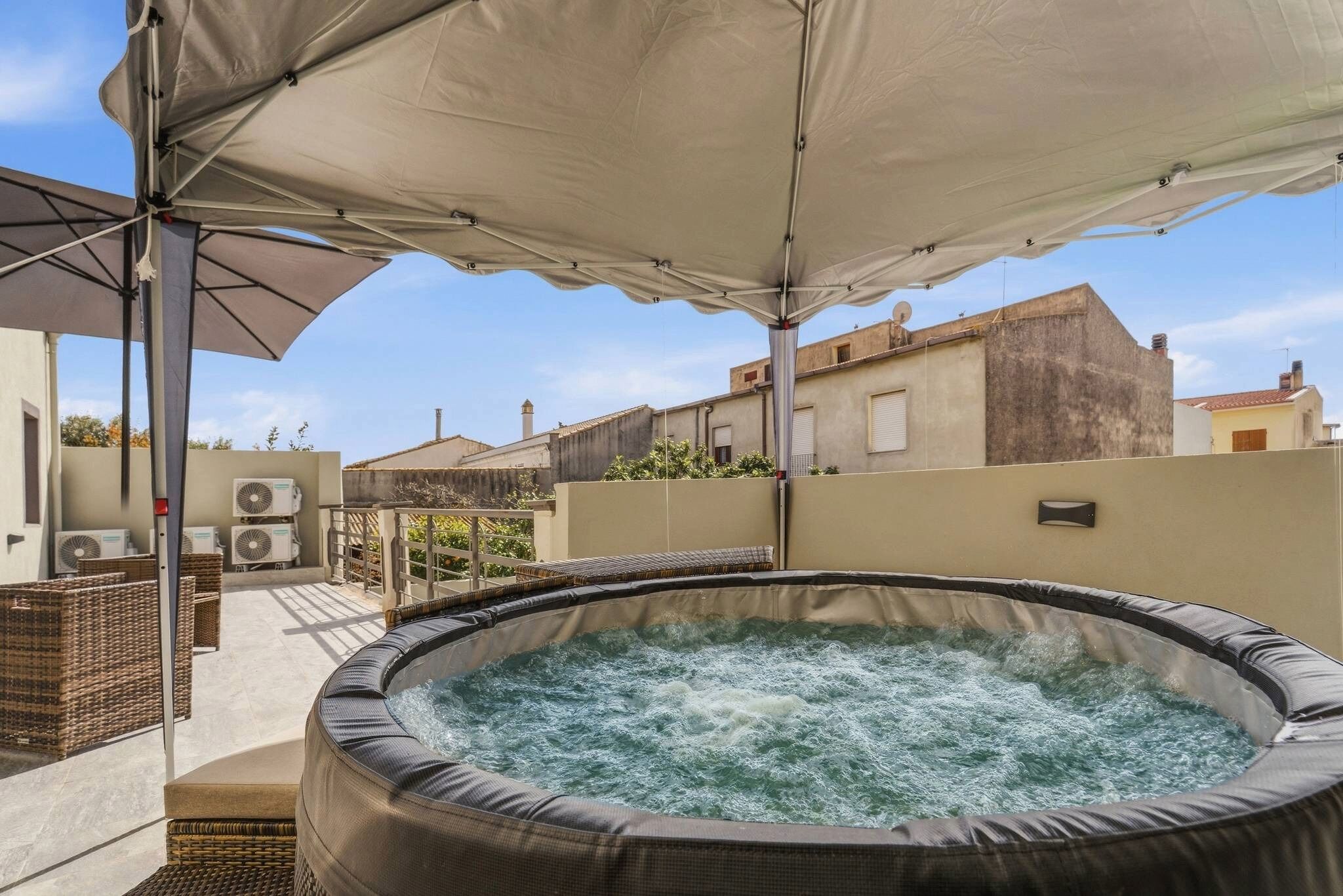 Un bain à remous installé sous une pergola, entouré de meubles en osier et de climatiseurs.