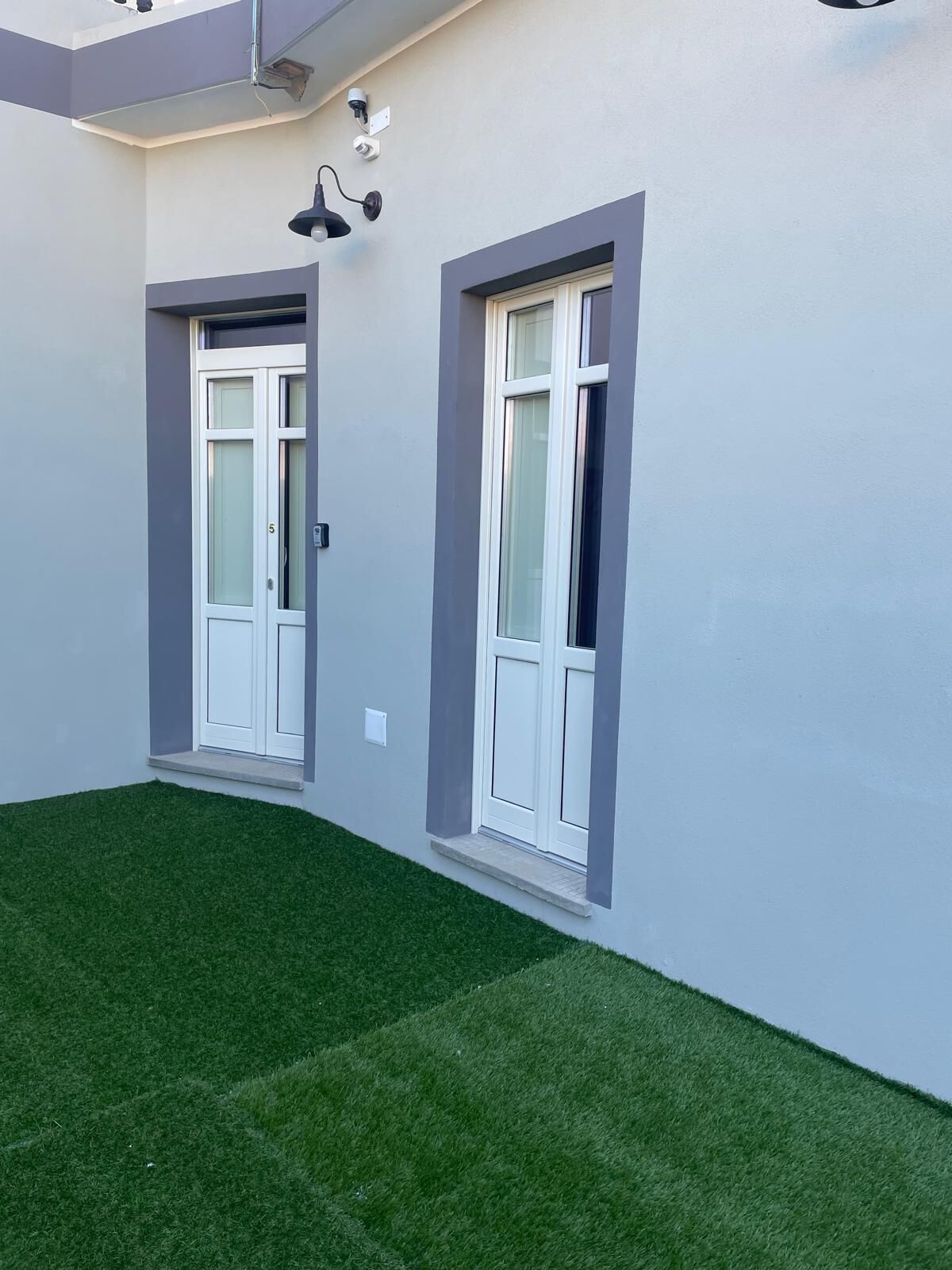 A modern building with two white-framed windows and a small balcony area with artificial grass.