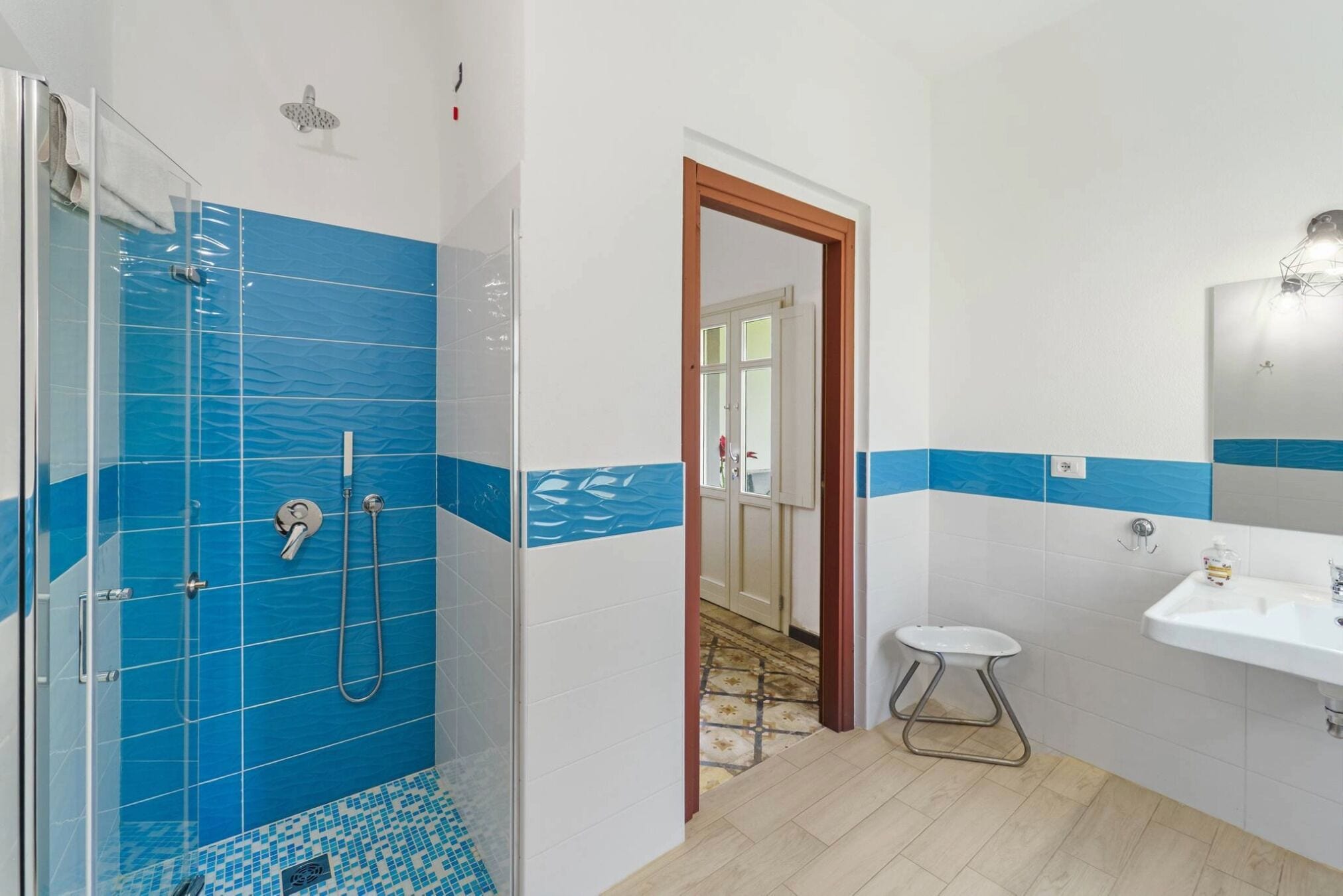 A bathroom with a glass shower enclosure, a sink, and a small stool.
