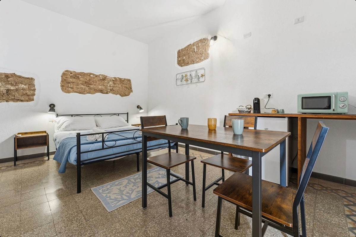 Ein kleines Zimmer mit einem Bett, einem kleinen Tisch, einem Stuhl, einer Mikrowelle und einer Kaffeemaschine.
