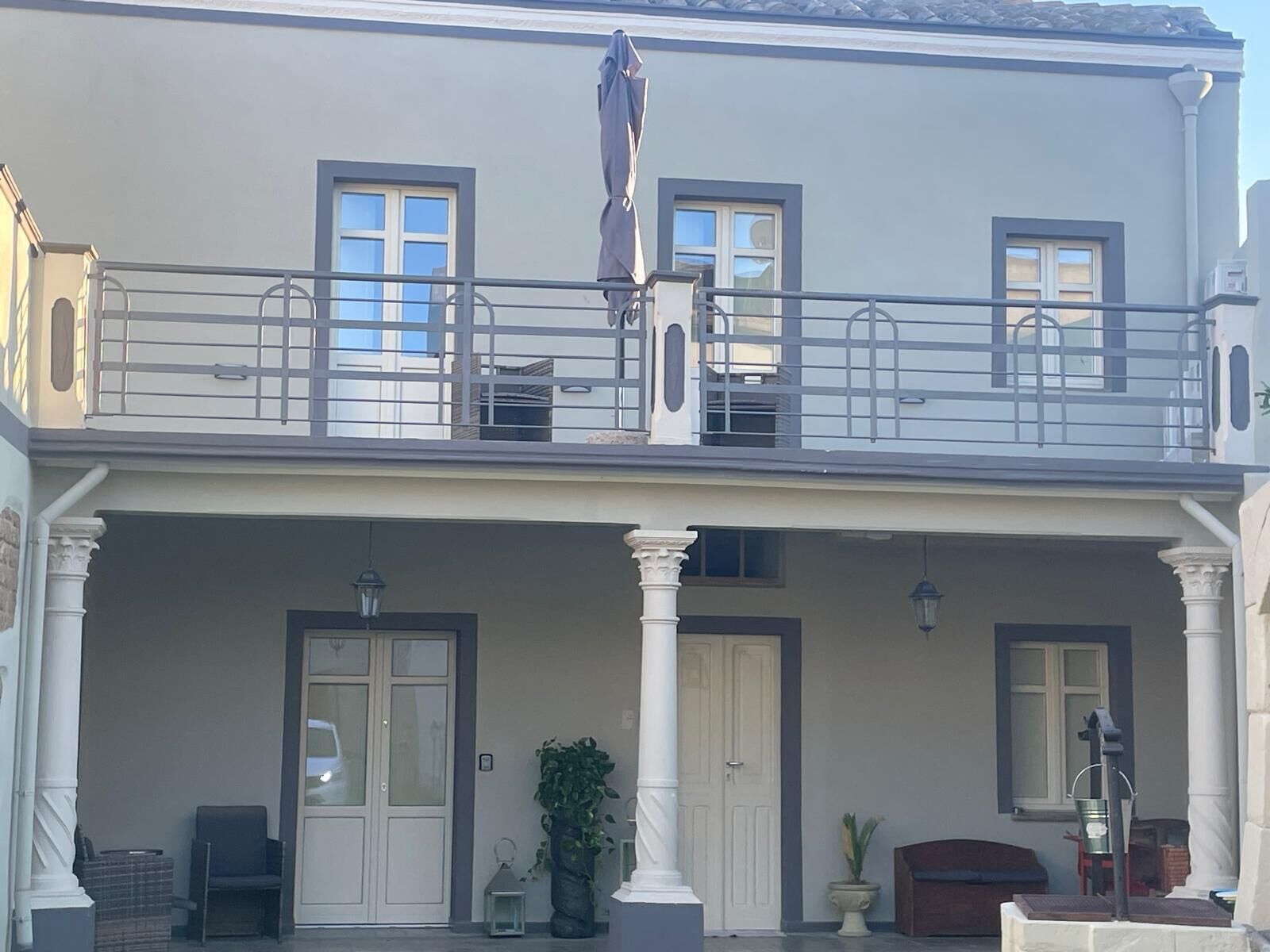 Un edificio de dos pisos con balcón, ventanas amplias y un porche cubierto.