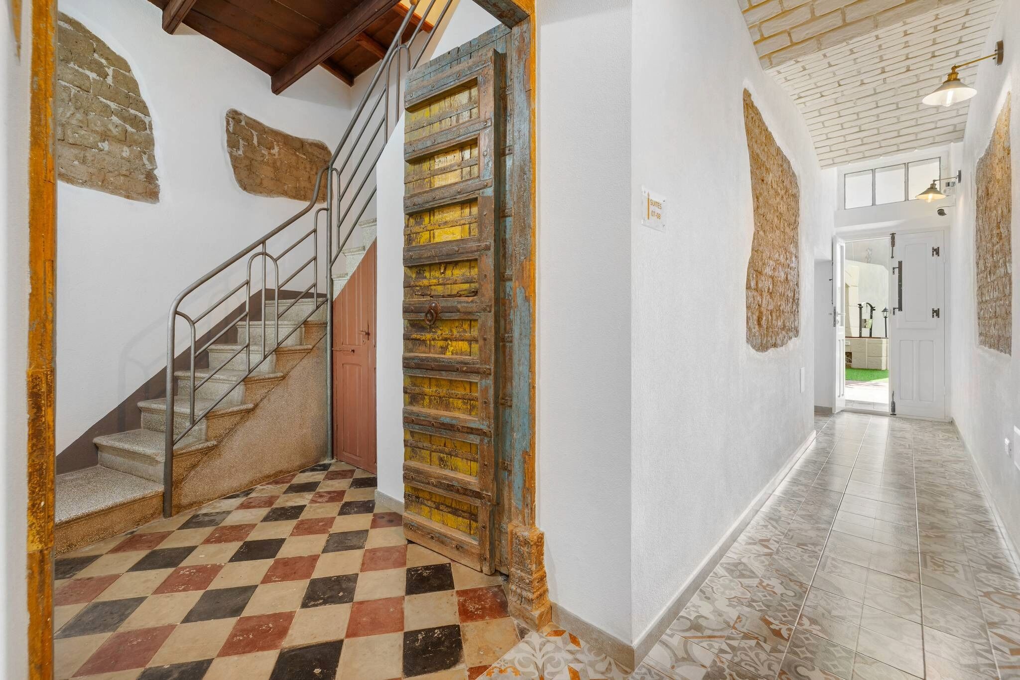 Un escalier avec une rampe en métal, un sol à carreaux et une porte rustique.