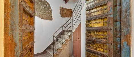 Una escalera con barandillas de metal, suelo a cuadros y puertas de madera rústica con pintura descascarada.