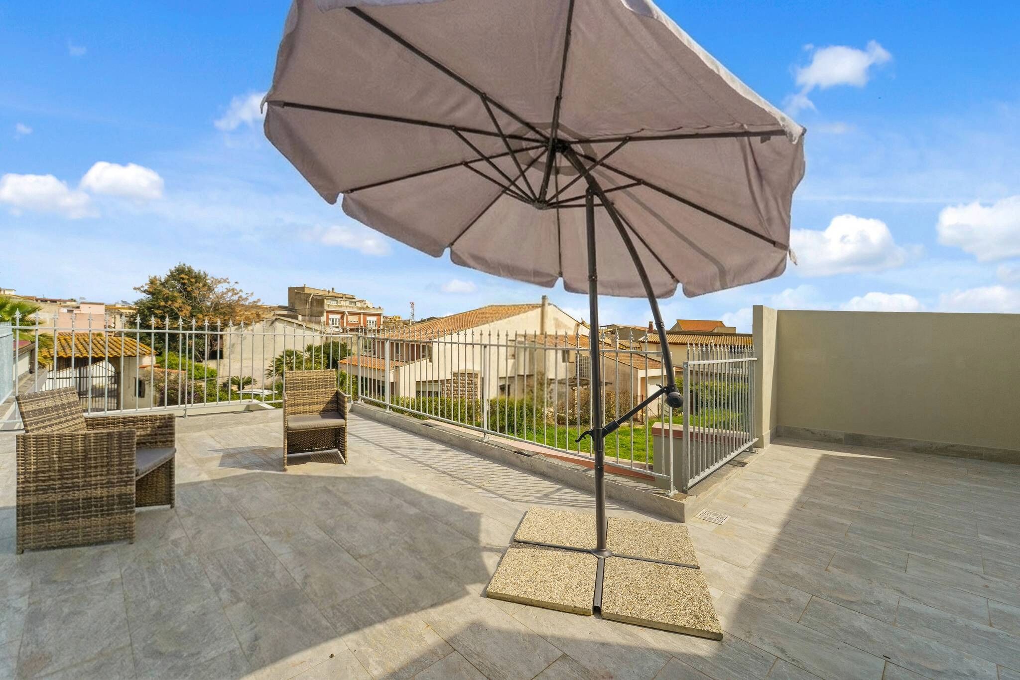 An outdoor patio with wicker furniture, a large umbrella, and a view of surrounding buildings.