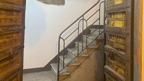 Una scala con ringhiera in metallo conduce a una stanza con pavimento a scacchi e un lampadario decorativo.