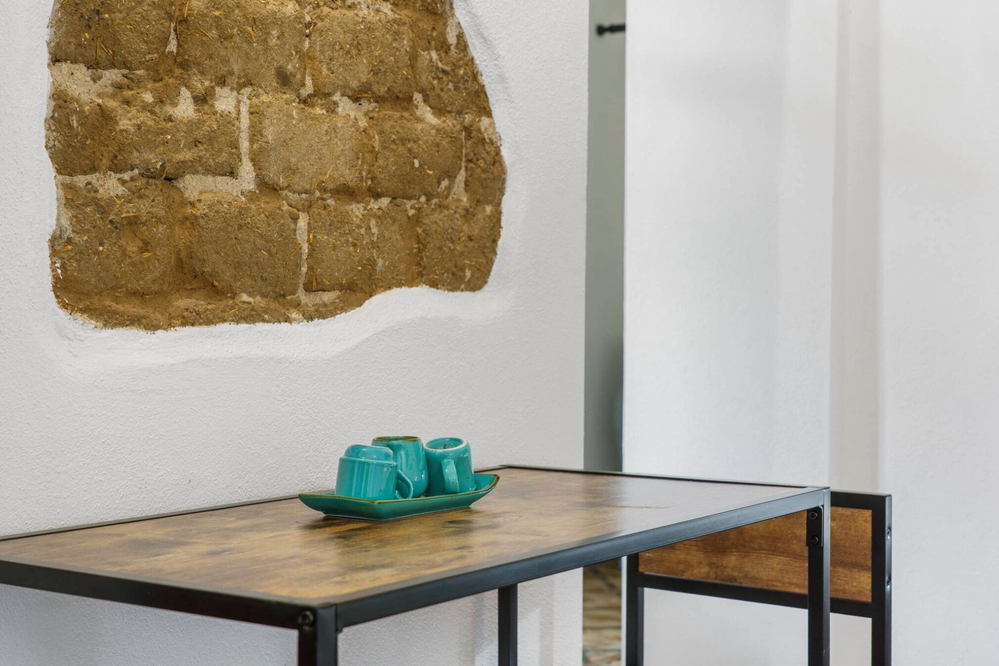Une table avec un bol de couleur turquoise et une chaise en bois, dans une pièce dont un mur est blanc et une partie est en briques.