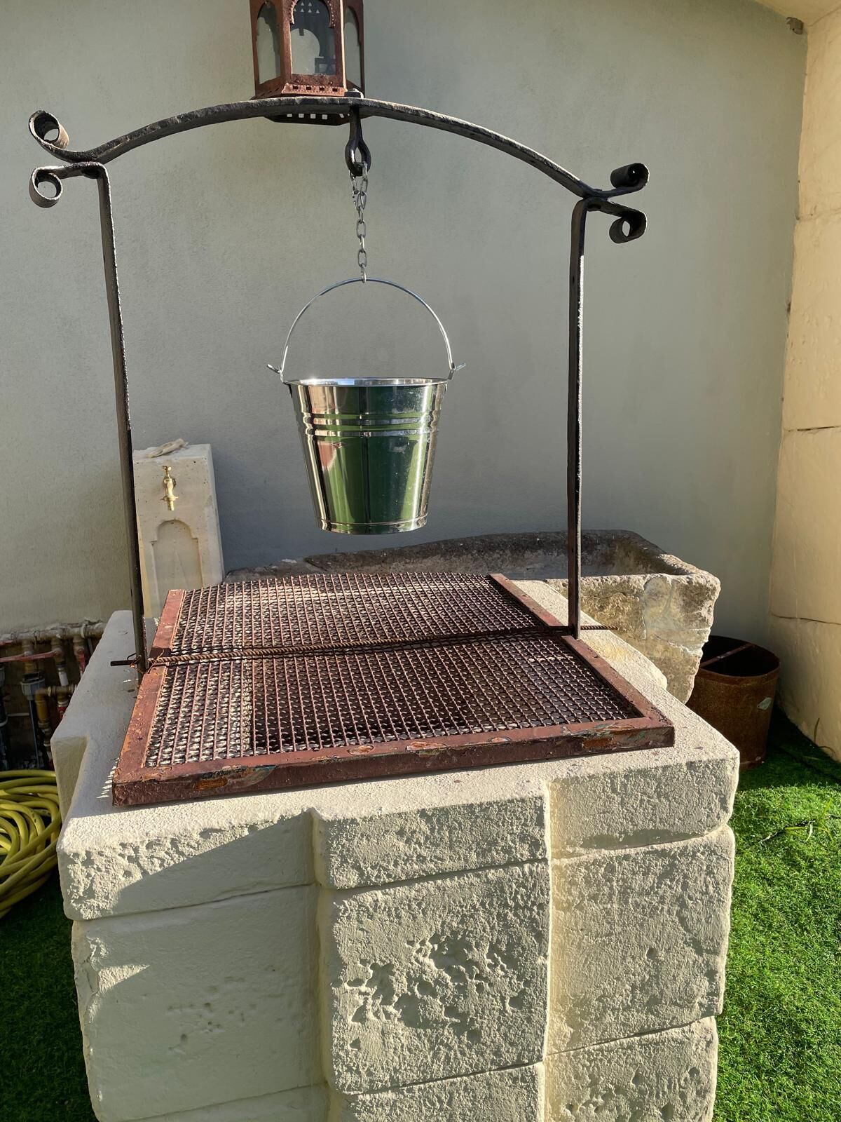 A metal grill with a metal bucket hanging above it, mounted on a stone structure.