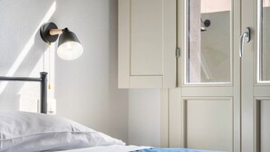 Un letto con biancheria bianca e blu, un lampadario a parete e una porta con maniglia.