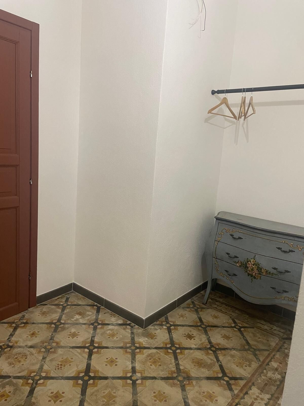 A corner room with a patterned tile floor, a wooden door, and a dresser with decorative elements.