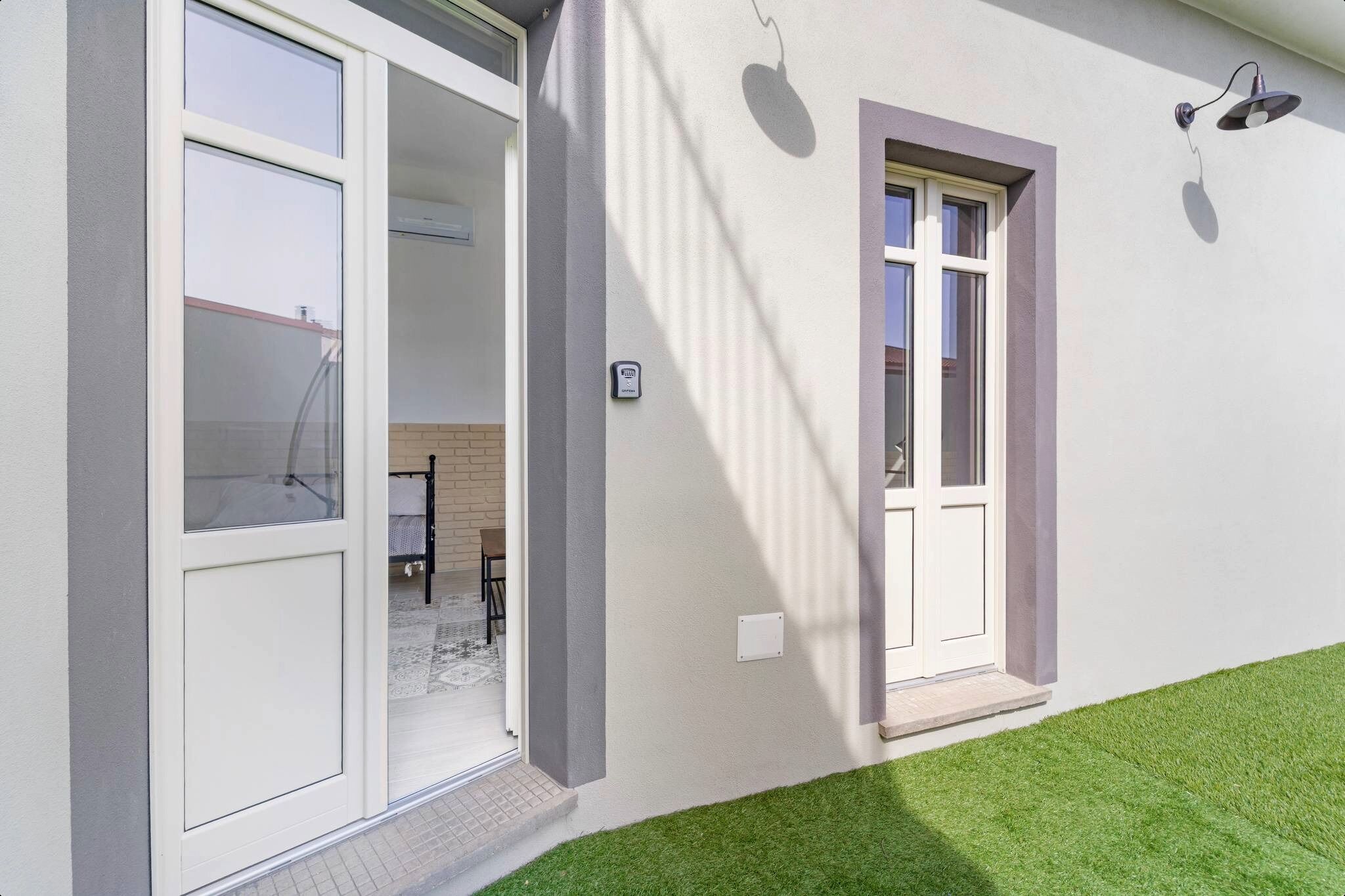 A modern building with a sliding glass door, a small window, and a wall-mounted light fixture.