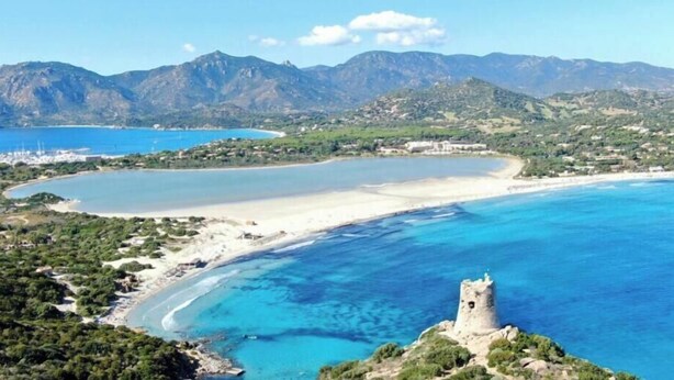 Paesaggio costiero con una torre, montagne e una spiaggia.