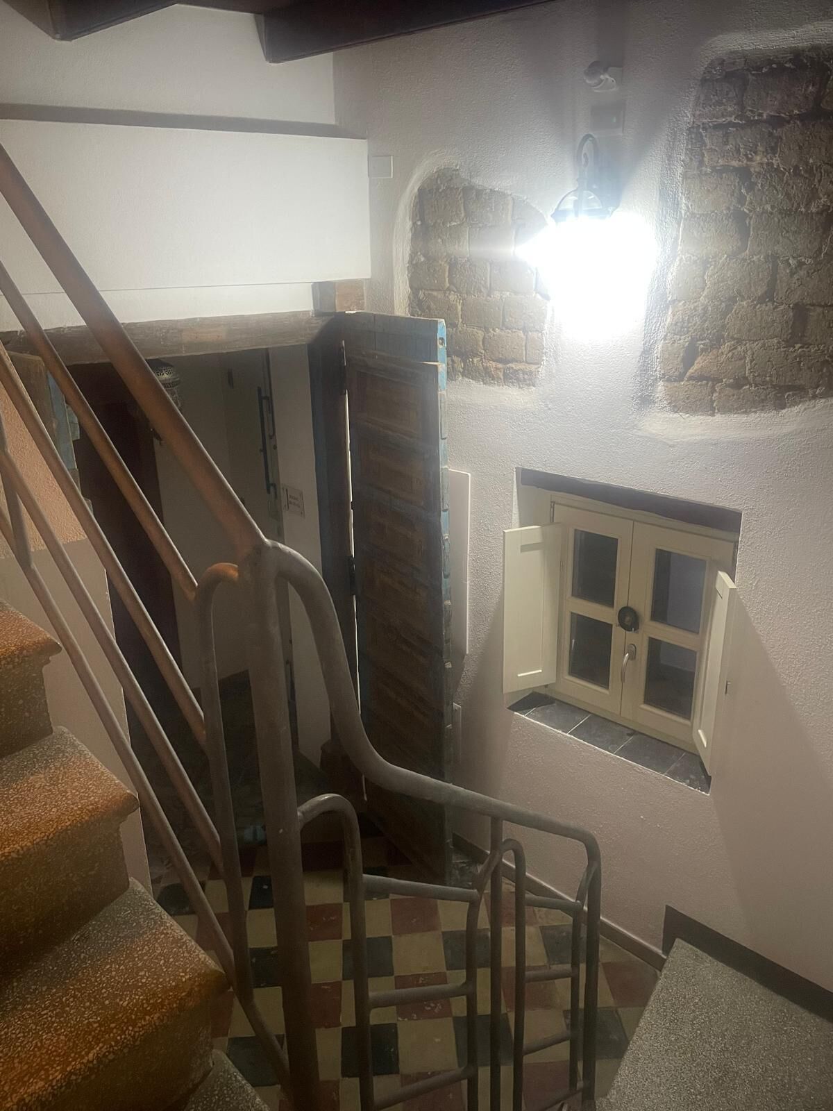 A staircase leading to a landing with a view of a stone wall and a door with glass panels.