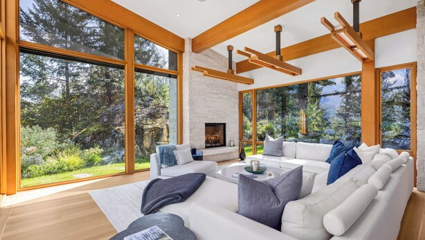 A modern living room with large windows, a fireplace, and a stone wall. - New luxury chalet with hot tub & media (Whistler)