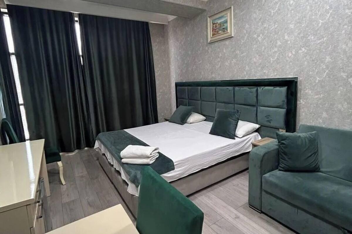 A hotel room with a bed, a green sofa, a desk, and a chair.
