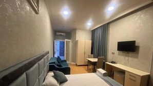 A hotel room with a bed, a desk, a TV, and a seating area. - Eleon Hotel (Baku)