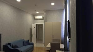 A hotel room with a blue sofa, a small table, a TV, and a wardrobe. - Eleon Hotel (Baku)