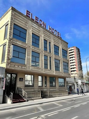 L’hôtel ELEON présente un bâtiment au style architectural classique, caractérisé par de grandes fenêtres et une entrée imposante.