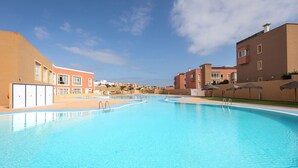 En stor, klar swimmingpool med flere baner, omgivet af bygninger med balkoner og en blå himmel.