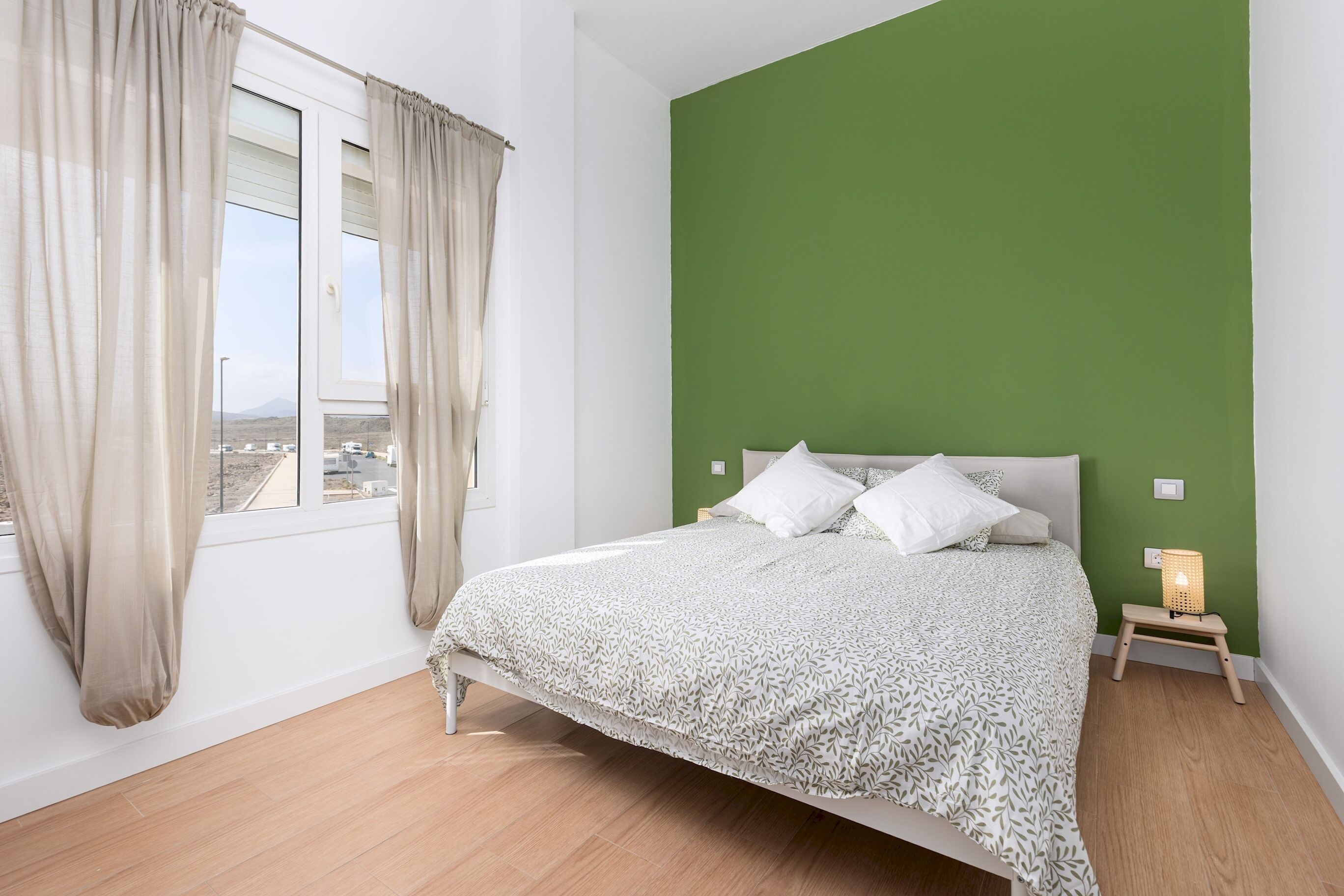 A bedroom with a bed, curtains, a nightstand, and a green wall.