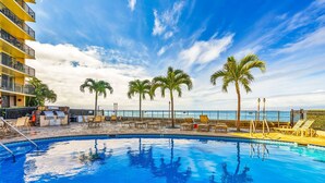 A swimming pool with lounge chairs and palm trees, overlooking a body of water. - Panoramic Oceanfront View, Breathtaking Sunsets, Relax on Large Lanai (Lahaina)
