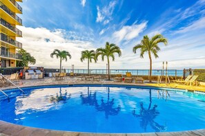 A swimming pool with lounge chairs and palm trees, overlooking a body of water. - Panoramic Oceanfront View, Breathtaking Sunsets, Relax on Large Lanai (Lahaina)