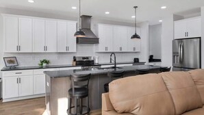 Une cuisine moderne avec des armoires blanches, un réfrigérateur en acier inoxydable et deux suspensions lumineuses.