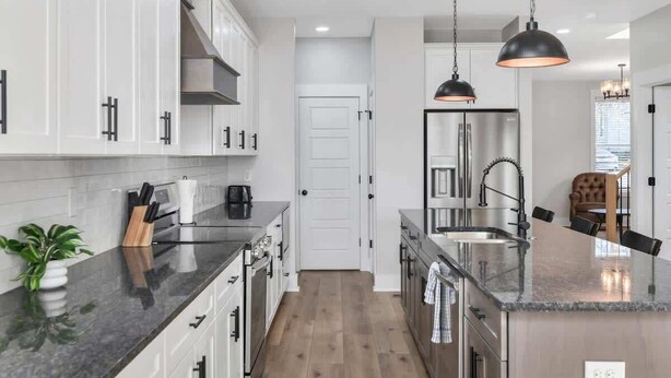 Une cuisine moderne avec des meubles blancs, un îlot central doté d’un évier et des luminaires suspendus.