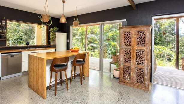 Eine moderne Küche mit einer Holzinsel, Barhocker und einem großen Fenster mit Blick auf Grünflächen.