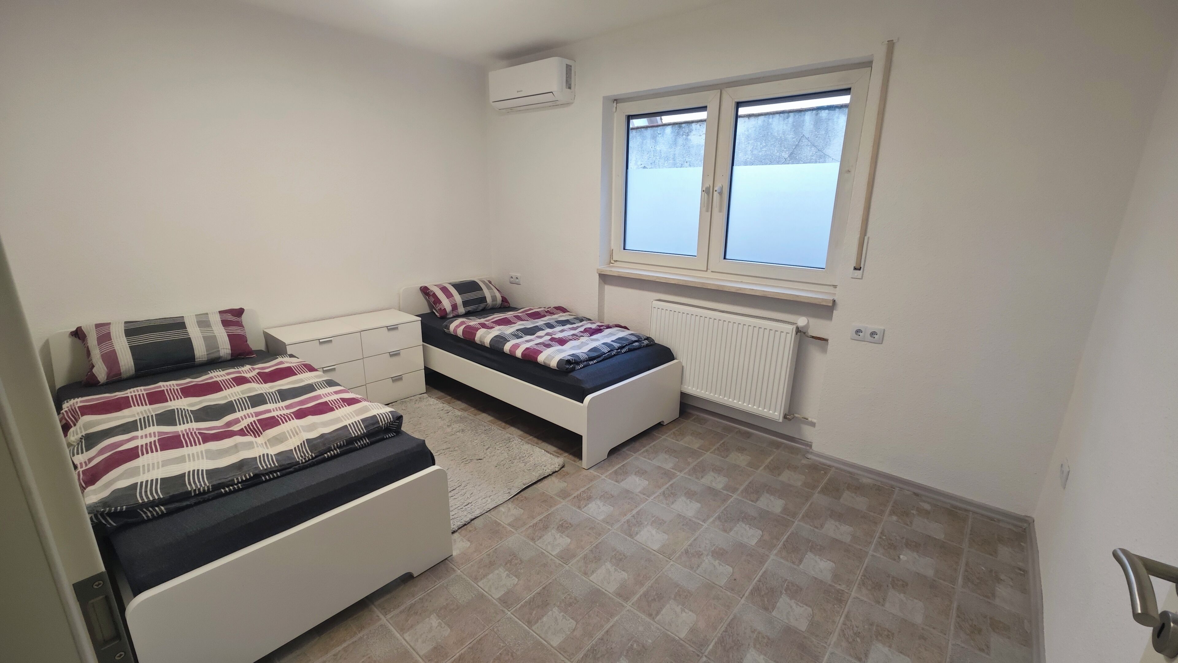A small, clean room with two beds, a window, and a radiator.