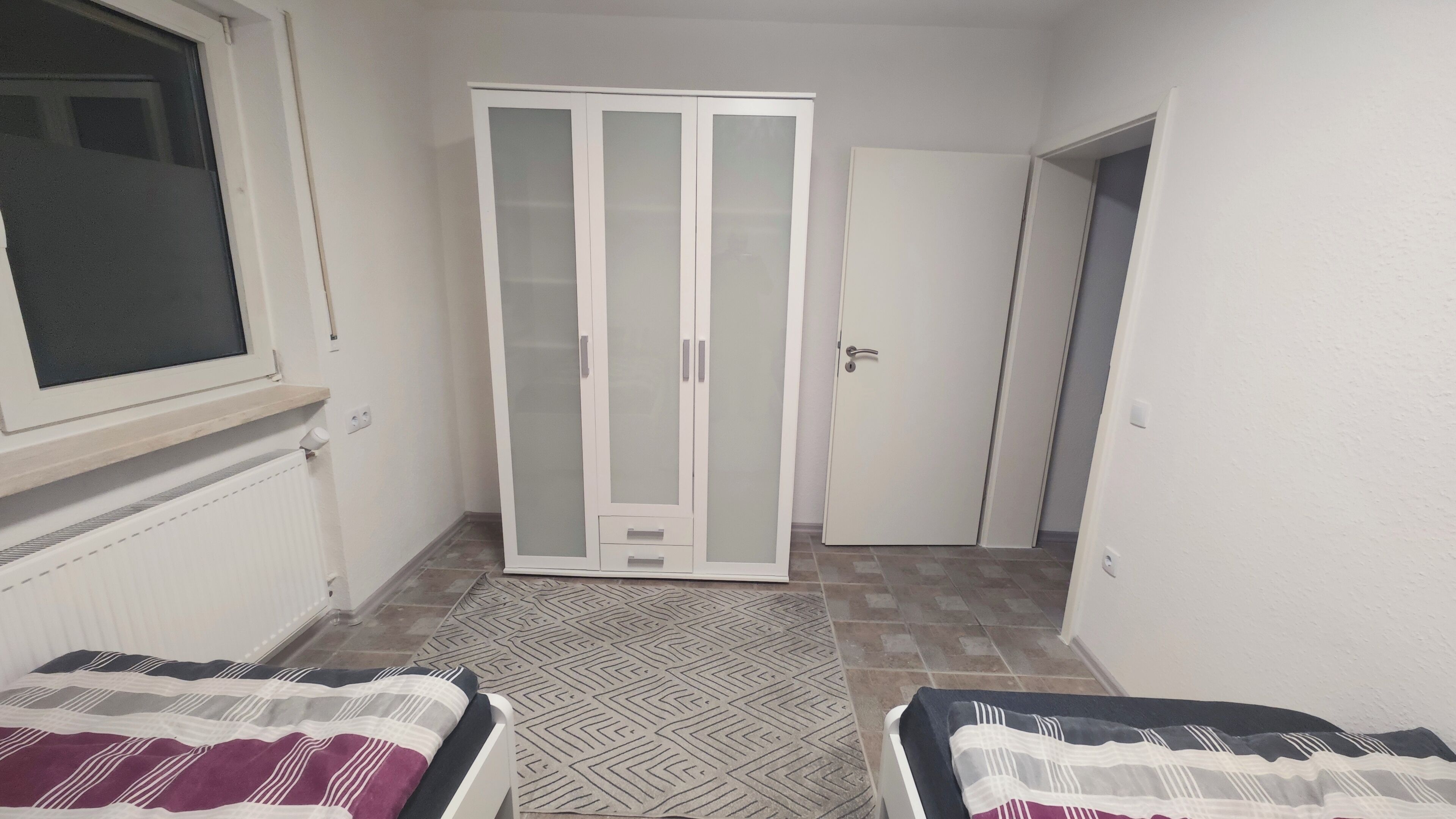 A small, narrow room with a wardrobe, a bed, and a radiator.