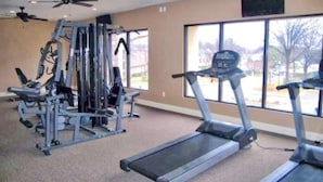 Un gimnasio con cintas de correr, máquinas de pesas y ventiladores de techo.