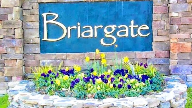 Un cartel con la palabra 'Briargate' sobre una pared de piedra y un parterre de flores debajo.