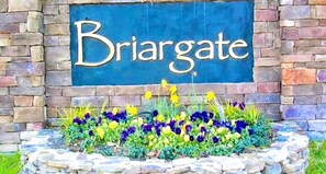 Une pancarte indiquant « Briargate » est fixée au-dessus d’un mur de pierre, et un parterre de fleurs se trouve en contrebas.