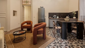 Een compacte woonruimte met kitchenette, een eethoek met tafel en stoelen, en een zithoek met een bank en fauteuils.