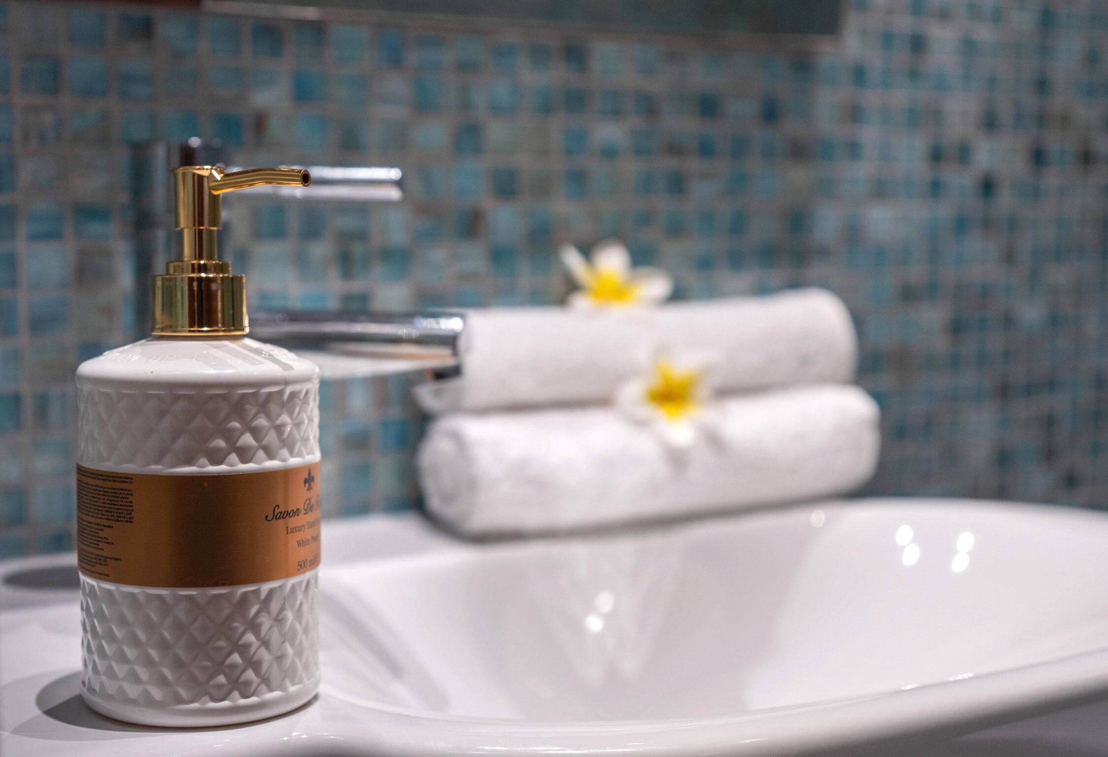A bathroom with a white sink, a gold faucet, and a textured soap dispenser.