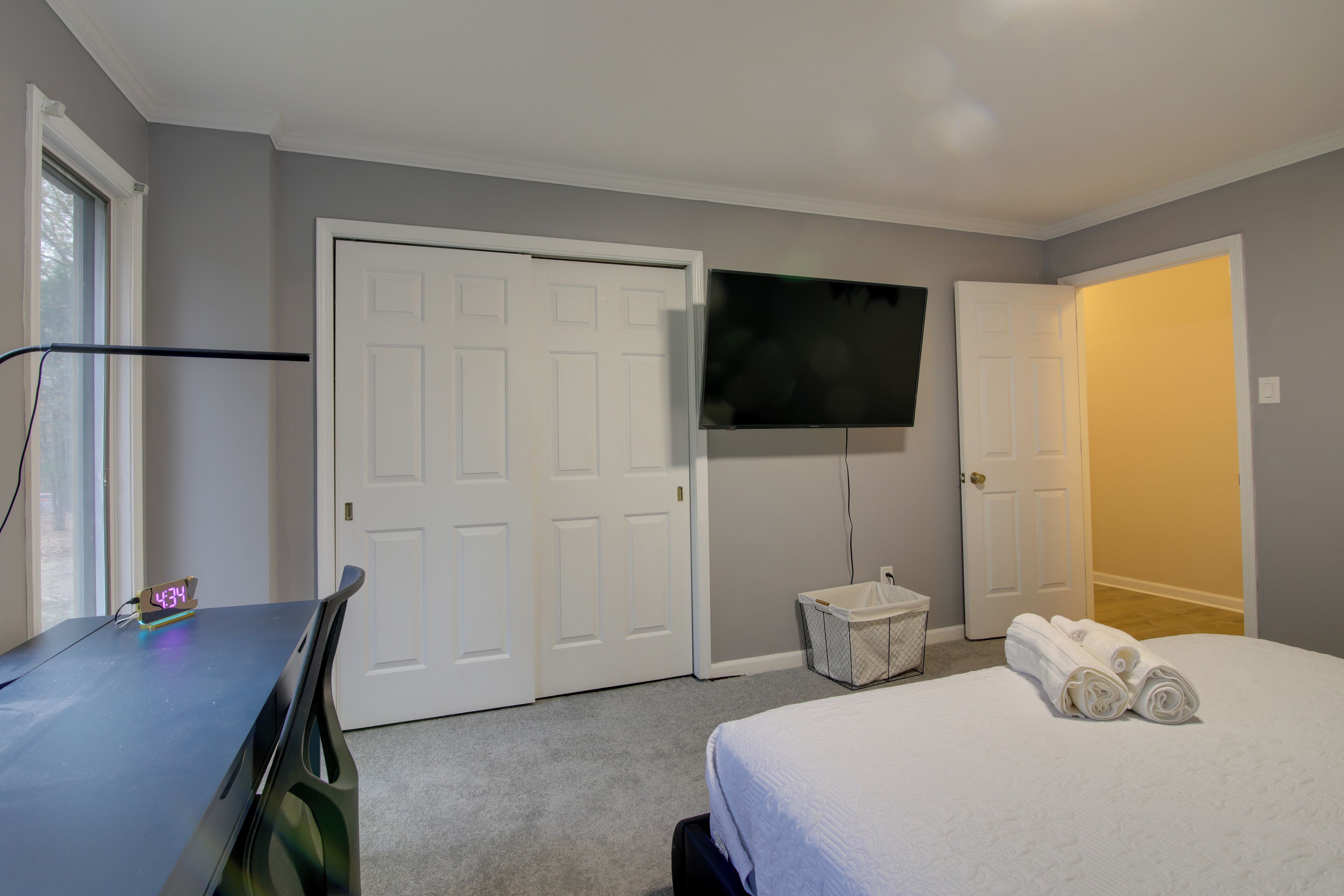 Habitación de hotel con cama, escritorio con computadora, televisor montado en la pared y puerta que da a otra habitación.