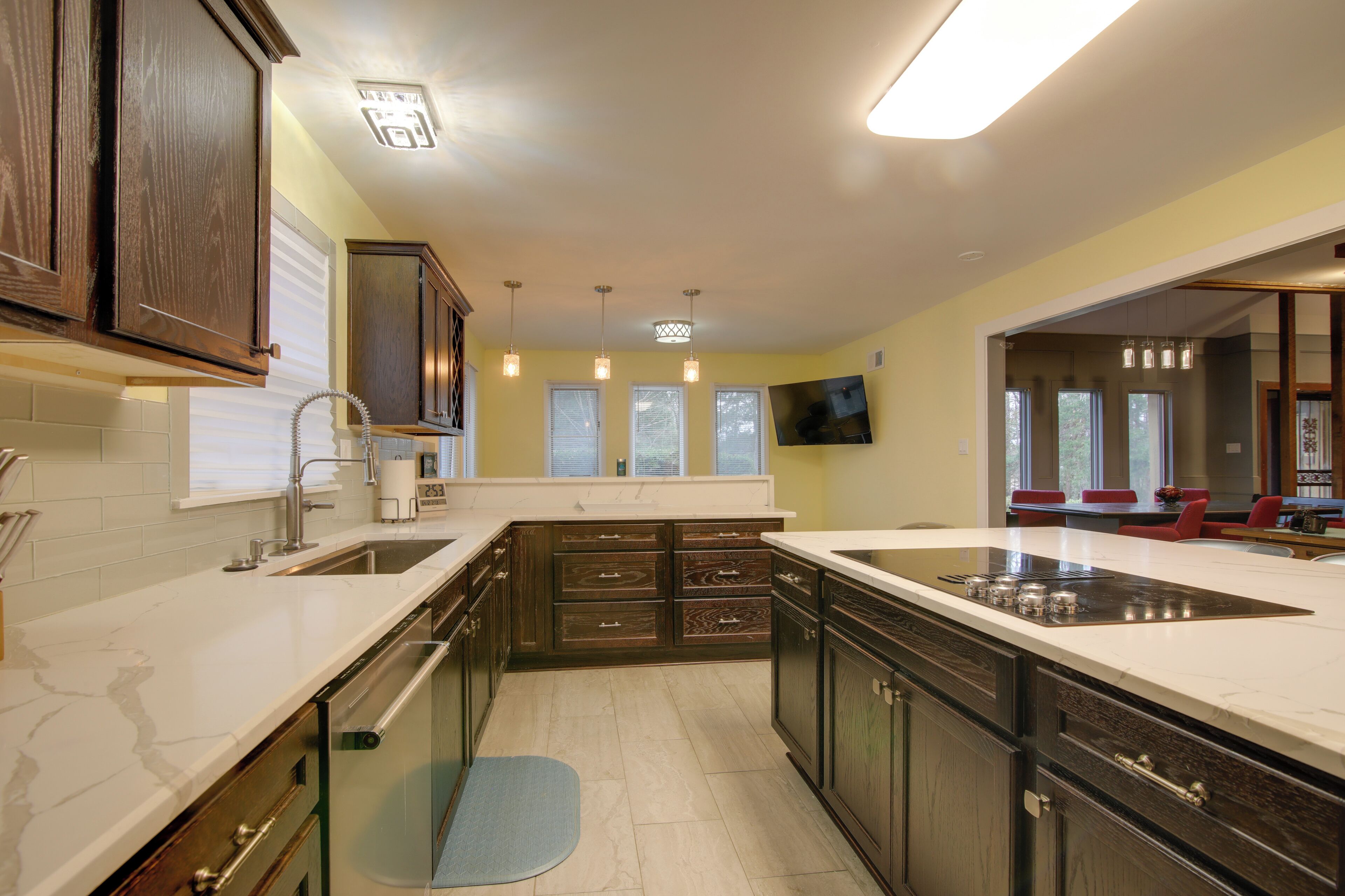 A modern kitchen with dark wooden cabinets, white countertops, and a large island.