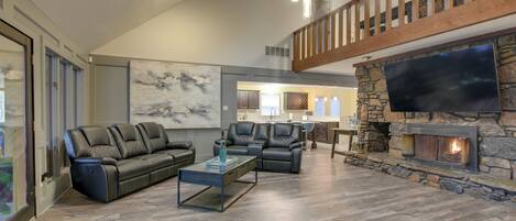 A spacious living room with a stone fireplace, leather sofas, and a large flat-screen TV.