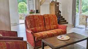 Ein geräumiger Wohnbereich mit einer Couch, Sesseln, einem Couchtisch und einer Treppe, die zu einem Außenbereich führt.