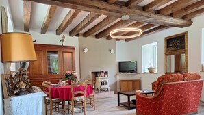 Ein Essbereich mit Holztisch und Stühlen, einem Fernseher und einer Couch in einem Raum mit freiliegenden Holzbalken und einem großen Spiegel.
