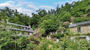 Ein Steinhaus mit geneigtem Dach, umgeben von dichtem Grün und Bäumen.