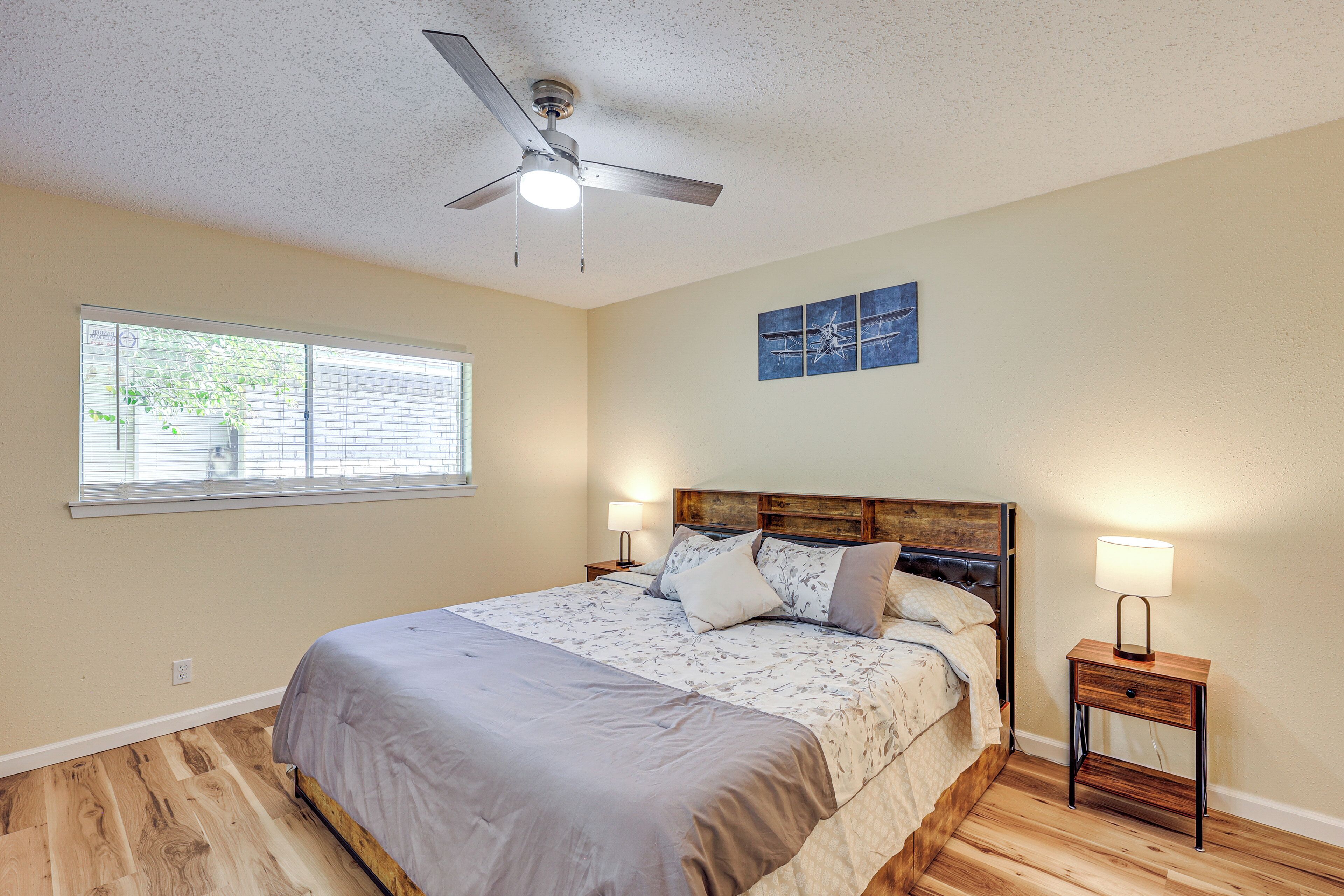 A bedroom with a bed, a ceiling fan, a nightstand with a lamp, and a window with blinds.