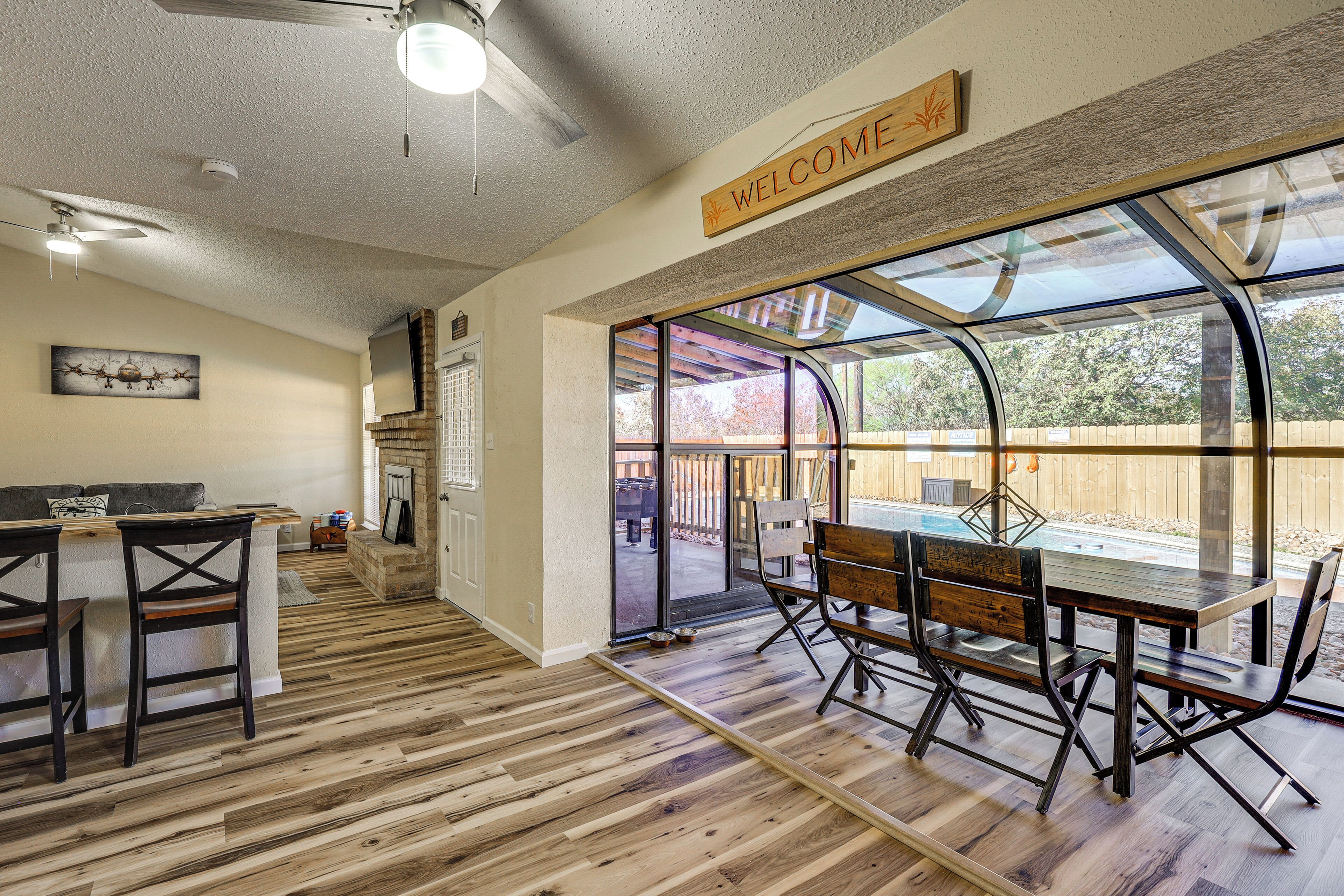 Amplia sala de estar con piso de madera, zona de bar y mesa de comedor con sillas. Hay un ventanal con vistas al exterior.