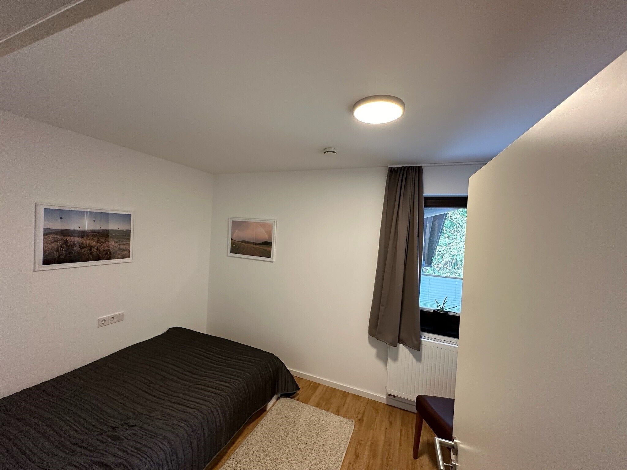 A bedroom with a bed, a window with curtains, and two framed pictures on the wall.