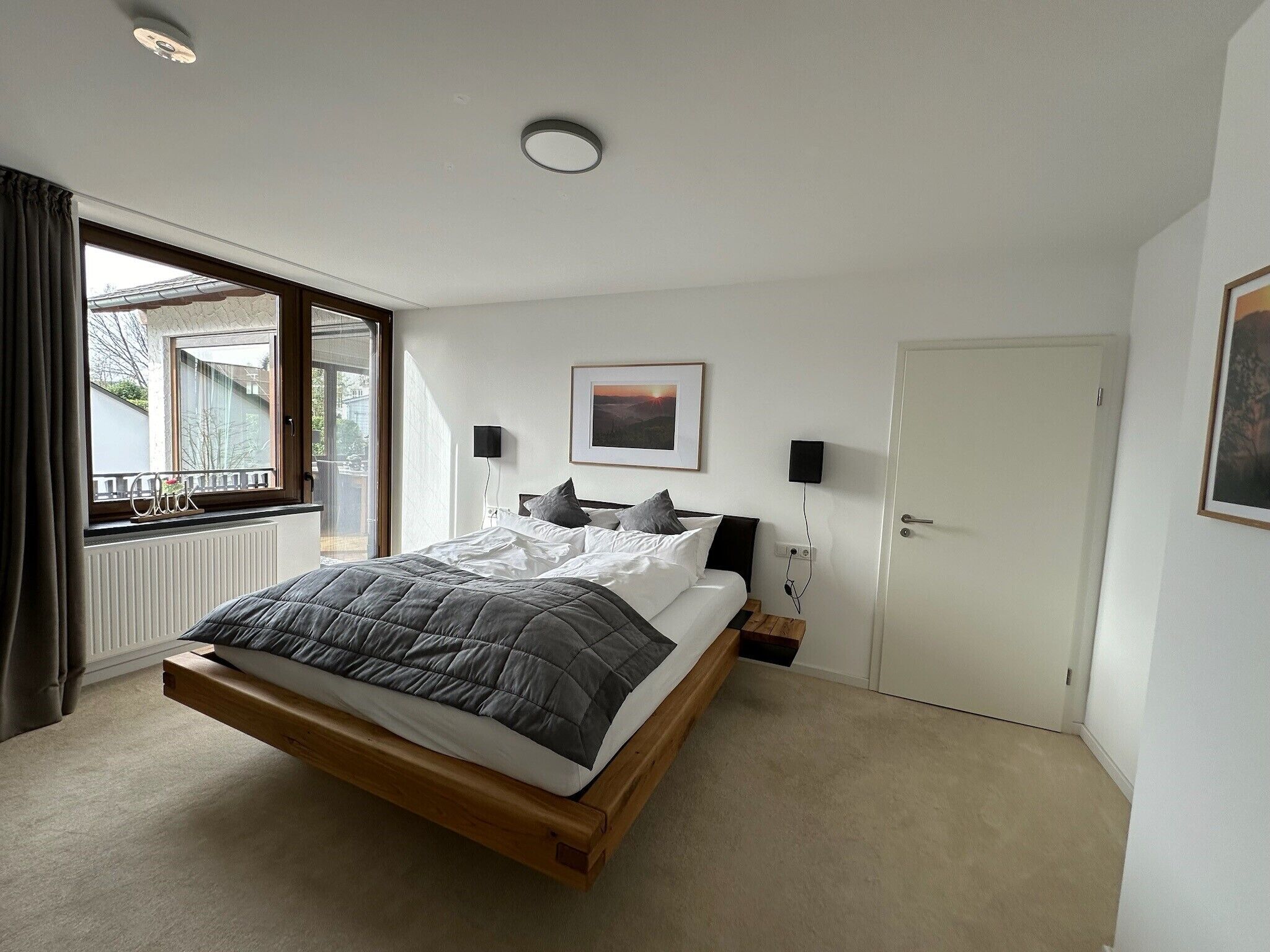 Ein Schlafzimmer mit Bett, Fenster, Tür und einem an der Wand hängenden Bild.