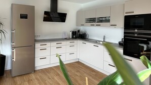 Eine moderne Küche mit weißen Schränken, einem Edelstahlkühlschrank, einer schwarzen Dunstabzugshaube und einem eingebauten Backofen.