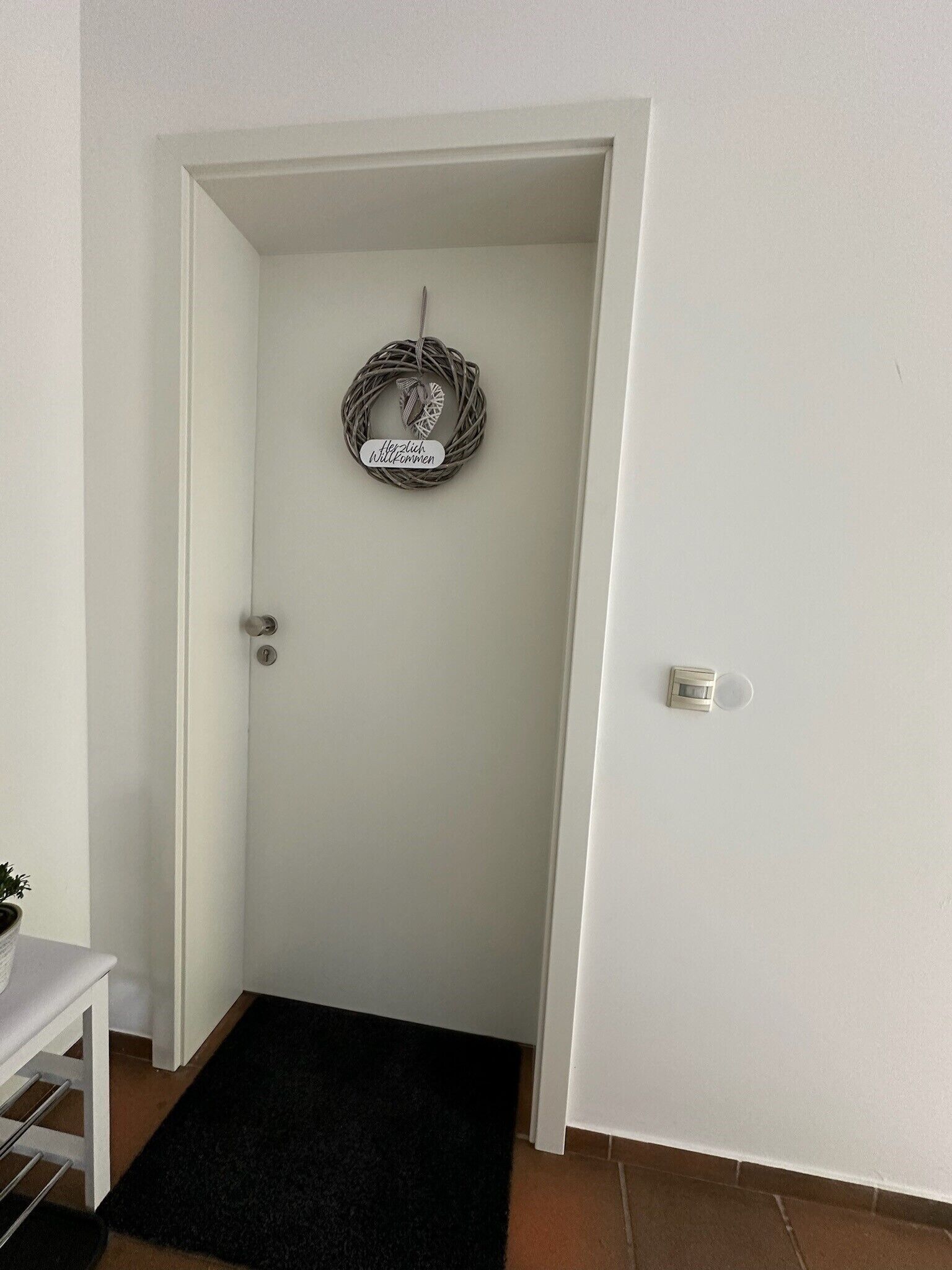 Une porte blanche, avec un paillasson et une enseigne suspendue.