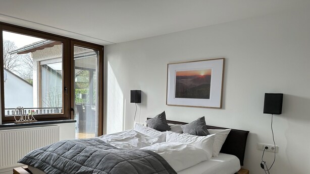 Ein Schlafzimmer mit Bett, Fenster, einem gerahmten Bild und Nachttischlampen.